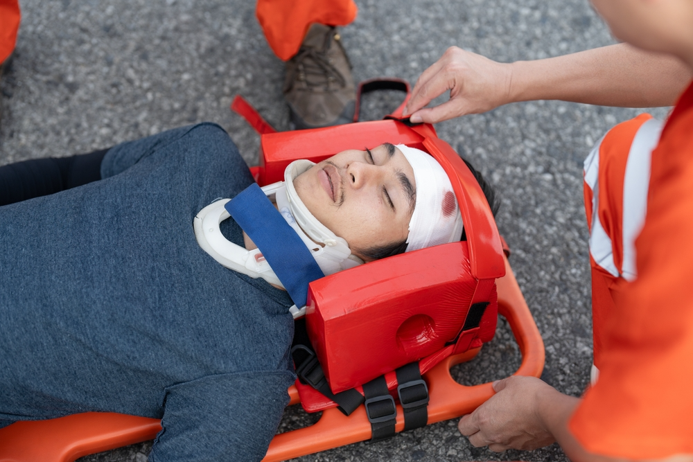 A man lies on a stretcher, showing signs of injury with a bandaged head, surrounded by medical personnel.