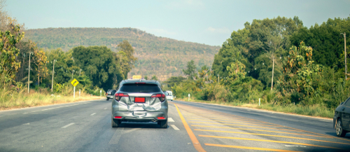 A car travels along a road, surrounded by lush trees in the background, showcasing a serene driving experience.