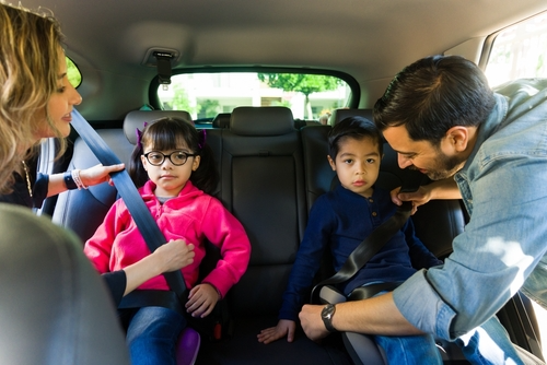 A group of people, including a boy and a girl, are seated in a car, all wearing seat belts for safety during their outing.