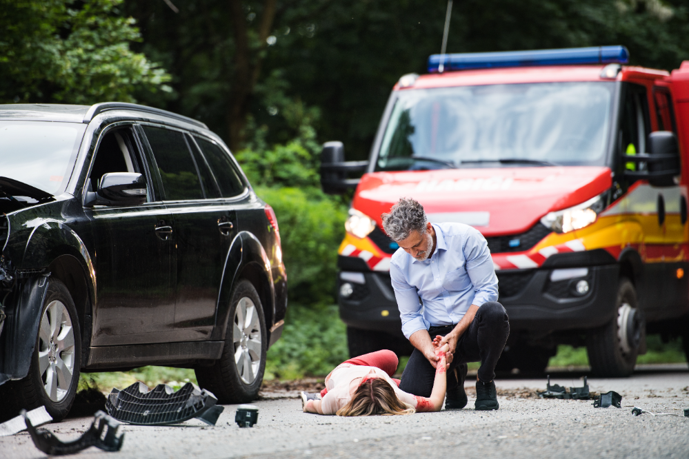 A man assists an injured woman on the ground after a car accident, showing concern and support in a critical moment.